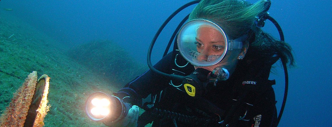 Una subacquea in immersione osserva un esemplare di Pinna nobilis illuminandolo con una torcia. Diventare subacquei nel migliore dei modi! Diventare subacquei nel migliore dei modi